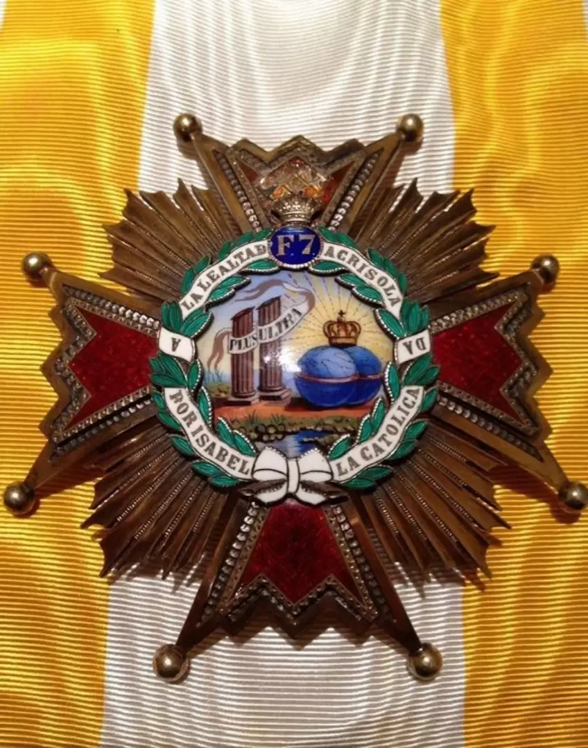 La Cruz de Oficial es una pieza esmaltada en blanco, con detalles dorados y una corona de laureles